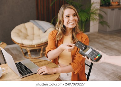 Young woman wearing shirt hold bank payment terminal to process acquire credit card pay bill sits alone at table in coffee shop cafe relax rest at restaurant. Freelance mobile office business concept - Powered by Shutterstock