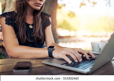 Young woman wearing smartwatch using laptop computer. Female working on laptop in an outdoor cafe.