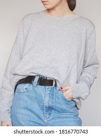 Young Woman Wearing Stylish Outfit With Grey Sweater And Blue High-waisted Mom Jeans Isolated On Light Grey Background. Copy Space