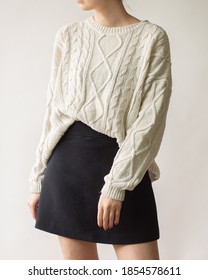 Young woman wearing stylish outfit with white chunky sweater and mini skirt isolated on white background.