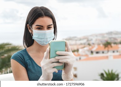 Young woman wearing surgical face mask using mobile smartphone o home terrace - Girl in quarantine Having fun video calling parents - Corona virus confinement and Youth millennial people concept - Powered by Shutterstock