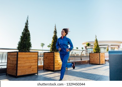 Young Woman Wearing Sweat Suit Jogging On Empty City Street In The Morning