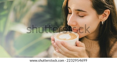 Young woman wearing sweater enjoying fresh hot cappuccino outdoors.
