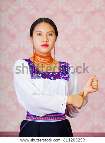 Young woman wearing traditional andean dress, facing camera doing sign language word for brother
