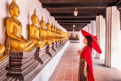 Young Woman Wearing Traditional Red Thai Dress And Golden Accessories Stands Holding A Traditional Umbrella In The Historical Site Wat Phutthaisawan Ayutthaya. Thai National Costume