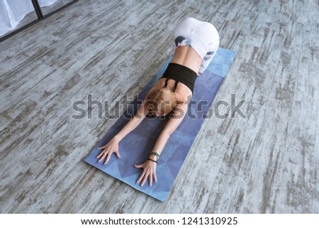 Young woman wearing training leggings and top working out against big window, doing yoga and pilates exercise, stretching. Healthy lifestyle and wellness