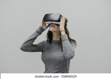 Junge Frau, die eine Virtual-Reality-Vorrichtung auf grauem Hintergrund trägt. Hände hoch