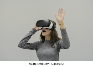 Junge Frau, die eine Virtual-Reality-Vorrichtung auf grauem Hintergrund trägt.