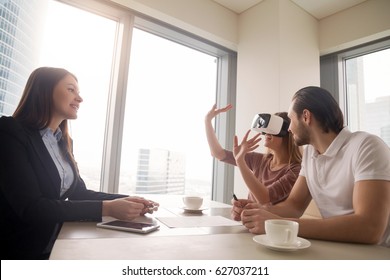Young woman wearing virtual reality glasses or goggles, couple using head-mounted display for real estate tours, excited by participation effect, virtually discover new flat, buy and sell homes in VR 