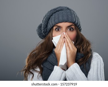 Young woman wearing warm hat sneezing