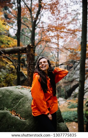 Young woman wearing warm orange sweater in the autumn forest. Misty landscape with mossy rocks. Cute smiley woman in the nature. Autumn forest hiking