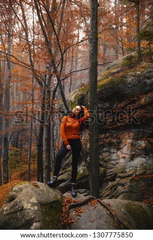 Young woman wearing warm orange sweater in the autumn forest. Misty landscape with mossy rocks. Cute smiley woman in the nature. Autumn forest hiking