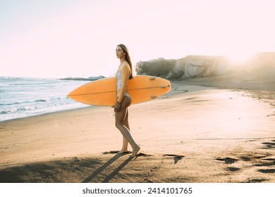 Young woman wearing wetsuit carrying surfboard at beach during sunset - Powered by Shutterstock