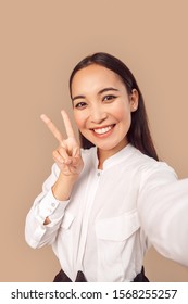Young woman wearing white shirt with dark long hair standing isolated on bage background taking selfie photo talking on smartphone smiling cheerful close-up