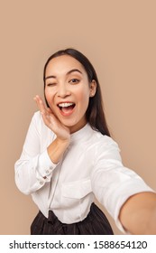 Young woman wearing white shirt with dark long hair standing isolated on bage background taking selfie photo winking to camera posing smiling playful