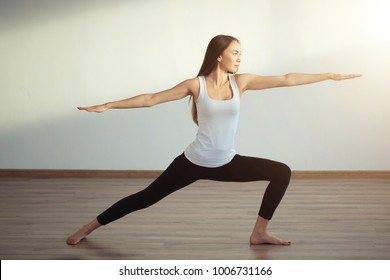 young woman wearing white tank top doing yoga exercise. Standing in Warrior one pose, Virabhadrasana