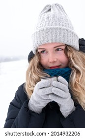 Young woman wearing winter clothing is enjoying hot tea from thermos mug outdoors. Winter travel. Keeping warm in cold weather