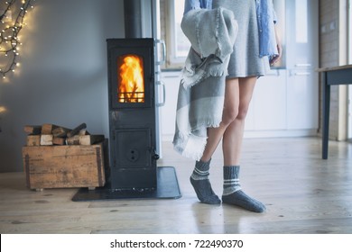 Young Woman Wearing Winter Socks Standing Home Holding A Blanket By The Fireplace. Wooden Cabin Interior. 