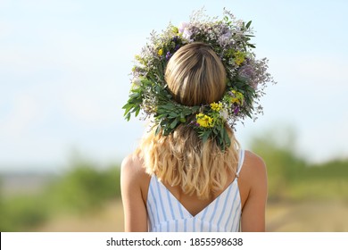 Young Woman Wearing Wreath Made Of Beautiful Flowers Outdoors On Sunny Day, Back View