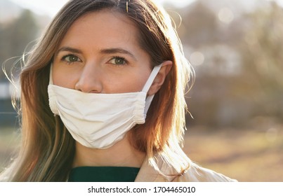 Young woman wears home made white cotton virus mouth face mask, wrong way, incorrect wearing - masks should cover nose as well