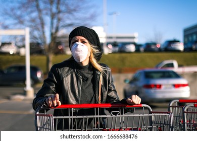 A young woman wears an N95 respirator mask while pushing a shopping cart outside of a grocery store. The woman is protecting herself from coronavirus and other airborne particles and diseases. 