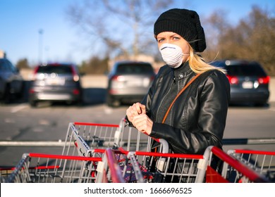 A young woman wears an N95 respirator while leaning on a shopping cart outside of a grocery store. The woman is protecting herself from coronavirus and other airborne particles and diseases. 