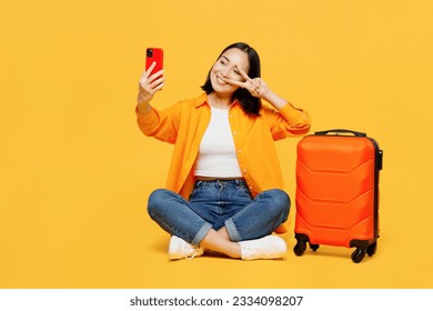 Young woman wears summer clothes sit suitcase do selfie shot on mobile cell phone isolated on plain yellow background. Tourist travel abroad in free time rest getaway. Air flight trip journey concept