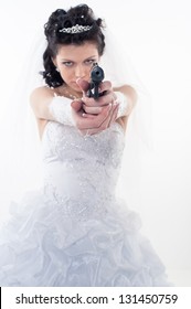 Young woman in a wedding dress with gun on a white background.A bride holding a gun pointing it at the camera. wedding. studio.