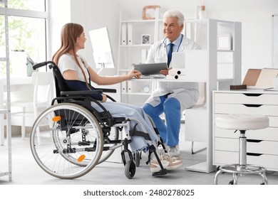 Young woman in wheelchair with broken arm visiting doctor at hospital - Powered by Shutterstock