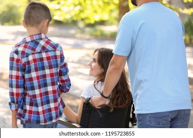 Young woman in wheelchair with her family walking outdoors - Shutterstock ID 1195723855