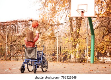 Young Woman In Wheelchair Playing Basketball On Autumn Day