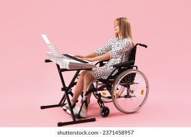 Young woman in wheelchair playing synthesizer on pink background