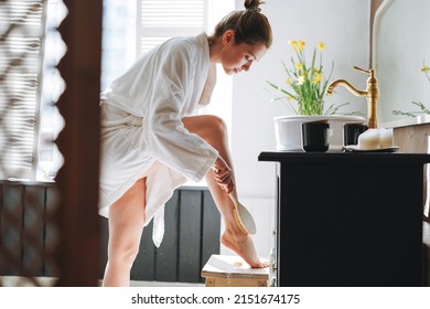 Young Woman In White Bathrobe Doing Body Massage With Dry Wooden Brush With Natural Bristles In Bathroom At Home