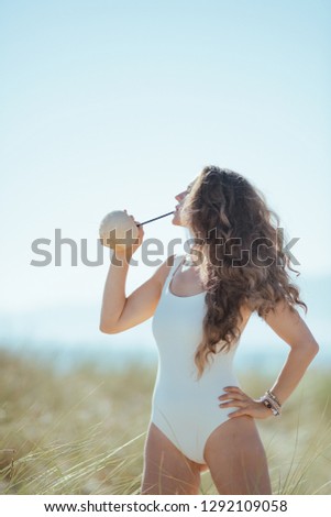 young woman in white beachwear on the ocean shore drinking from coconut. Coconut helps to increase energy by burning fat. blue sky. minimal to no crowd peace. quiet vacation heaven. european woman.