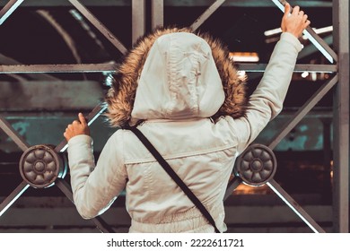 Young Woman In White Coat Stand In Front Of Border Fence, Rear View. Girl Is Waiting For The Passage At Night