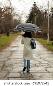 Young woman in a white coat with an umbrella walks in the park. Selective focus.