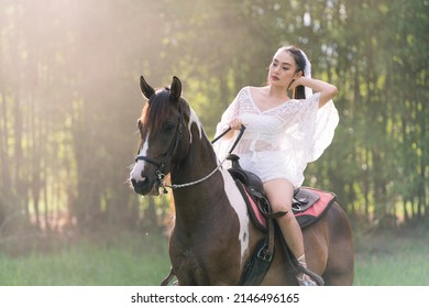 Young woman in white dress with horse. Woman riding red horse in the garden. Beautiful bride in a dress riding a horse.
