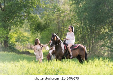 Young woman in white dress with horse. Beautiful woman riding a horse at sunset on the forest. Young beauty girl with a horse in the rays of the sun by the garden.