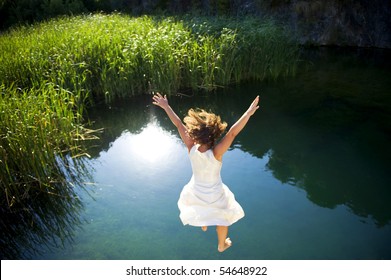 Young woman in white dress jumping into a idyllic lake