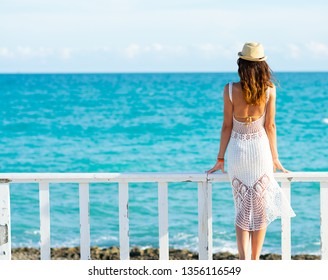 Young woman in white dress, sea and bright sky in the background

