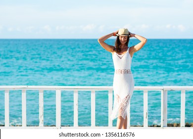 Young woman in white dress, sea and bright sky in the background
