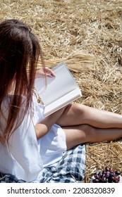 Young Woman In White Dress Sitting On Haystack In Harvested Field, Reading Blank Book. Book Mockup