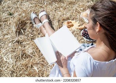 Young Woman In White Dress Sitting On Haystack In Harvested Field, Reading Blank Book. Book Mockup