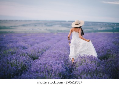 Young woman in a white dress and straw hat running in a lavender field with basket