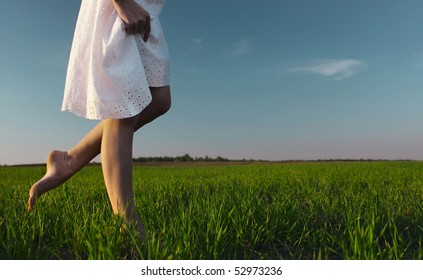 Young woman in white dress walking on meadow with green grass