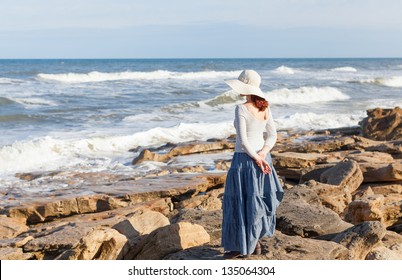 A young woman in a white hat is watching  waves.