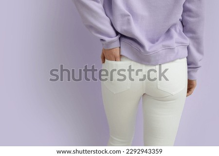 Young woman in white jeans on lilac background, back view