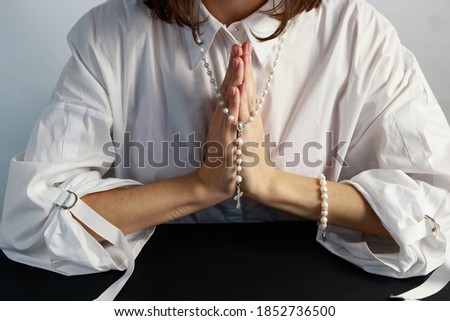 A young woman, in a white shirt folding a lodon to each other prays to God holding rosary. 