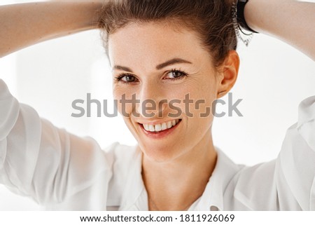 Young woman in white shirt on white background. Beautiful girl in white clothes sits on the floor on a white background. Studio shot.
