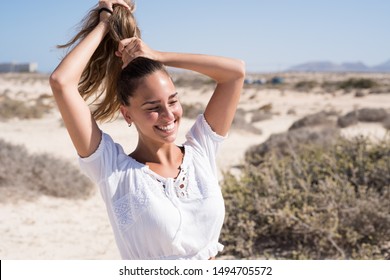 Young Woman In A White Shirt Is Standing On The Beach And Holding Her Hair Above Her Head In A Pony Tail